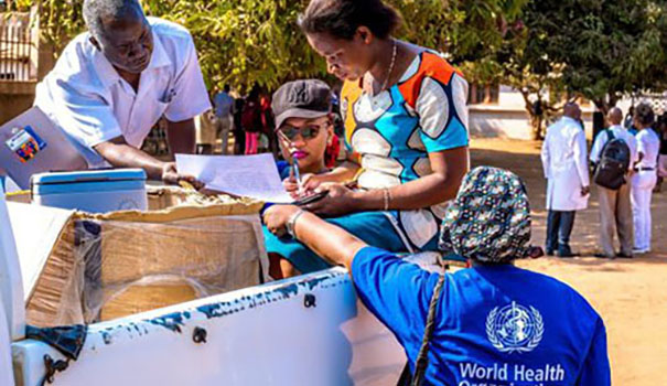 A doctor and staff checking medical documents in a lorry with a member from WHO standing by.