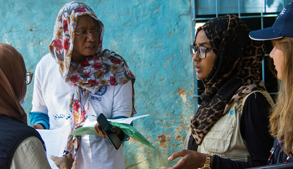 A female doctor from WHO discussing a patients file with female colleagues outside a hospital building.
